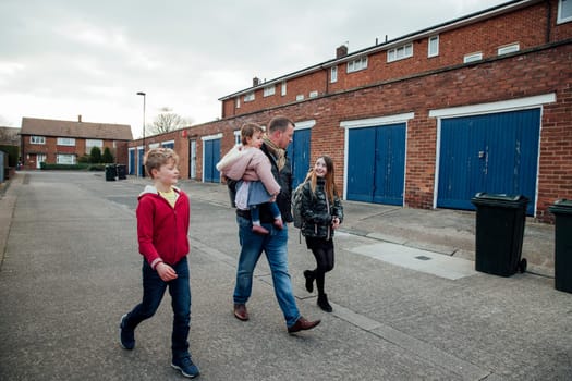 Mature man has just picked up his eldest daughter from school with his other two children. They are talking as they walk home together.