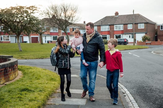 Mature man has just picked up his eldest daughter from school with his other two children. They are talking as they walk home together.