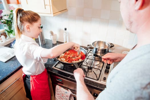 Little girl is learning how to cook with her father at home. They are making a spagetti bolognese together.