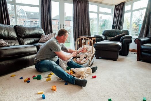 Stay at home father is relaxing in the living room with his baby daughter while she is in her baby bouncer.
