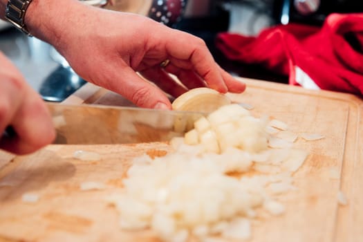 Close up shot of a mature man cutting up an onion on a chopping board inthe kitchen of his home.