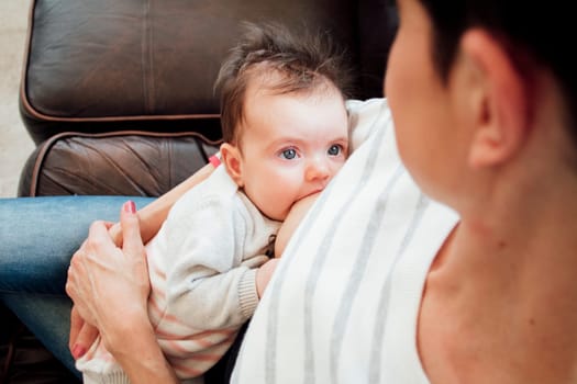 Newborn baby girl is looking at her mother while she breastfeeds her.