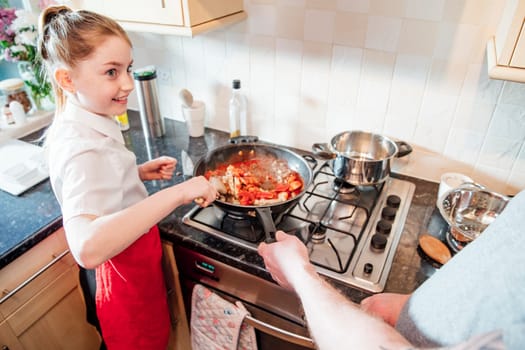 Little girl is learning how to cook at home with her father. They are making a spagetti bolognese together and she is stirring with a wooden spoon.