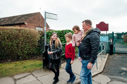 Mature man has just picked up his eldest daughter from school with his other two children. They are talking as they walk home together.