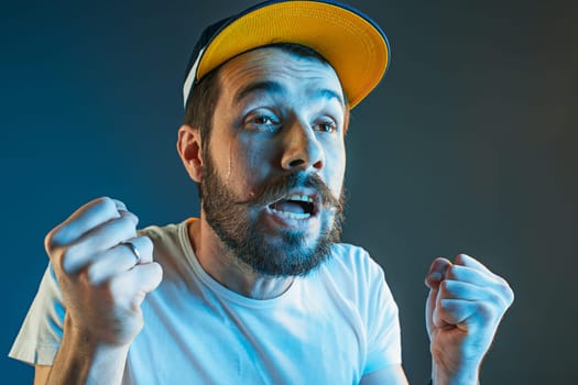 Sports, fan human emotions and people concept - sad young man watching sports on tv and supporting team at home. Crying emotional man screaming in colorful bright lights at studio. Facial expression concept.