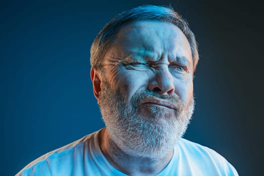 Sports, fan human emotions and people concept - sad senior man watching sports on tv and supporting team at home. Crying emotional man screaming in colorful bright lights at studio. Facial expression concept.