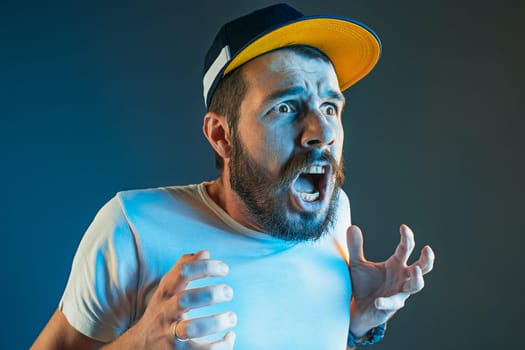 The anger and screaming man. Hate, rage. Crying emotional angry man in colorful bright lights at studio background. Emotional face. Fan human emotions, facial expression concept.
