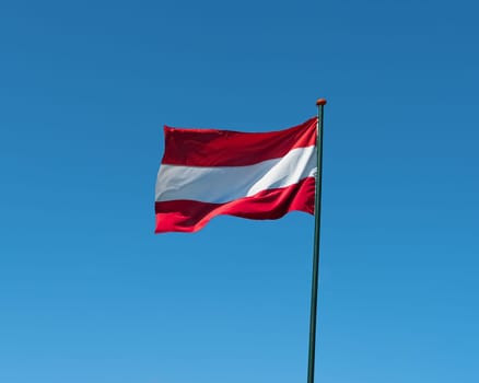Flag of Austria on flagpole waving in the wind. Austrian national official flag on blue sky background. Patriotic symbol, banner