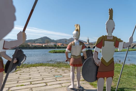 PONTE DE LIMA, PORTUGAL - CIRCA APRIL 2018: Statues of roman soldiers near Lima River at Ponte de Lima with San Antonio church on the background.