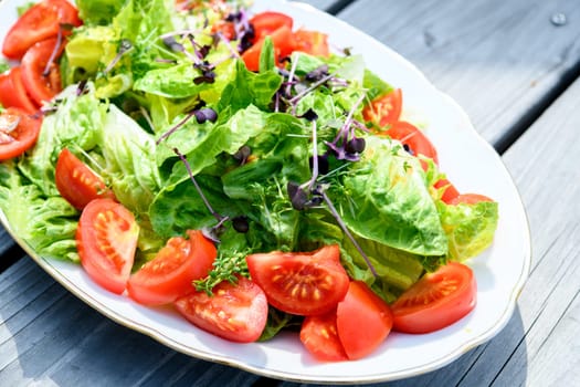 mixed summer salad on plate and wooden ground