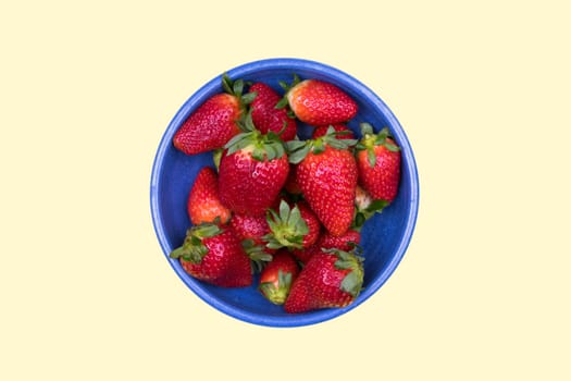 strawberries in blue bowl on pastel yellow ground from above