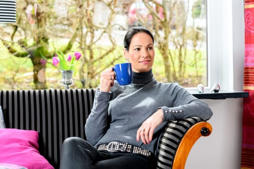 young dark haired woman at home with cup of coffeee relaxing