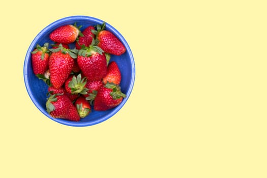 strawberries in blue bowl on pastel yellow ground from above