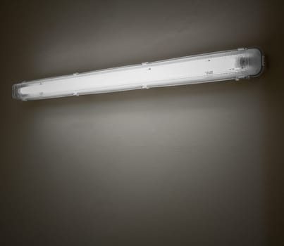 Old neon lamp illuminates, with weak light, a white concrete wall. Space for text.