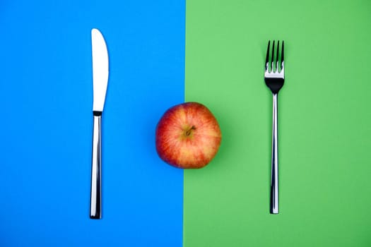 red apple from above with knife and fork on blue and green ground
