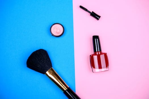 makeup collection with  mascara, nail polish ,eye shadow and brush from above on blue and pink ground
