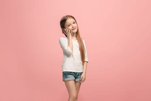 Happy teen girl standing, smiling with mobile phone over trendy pink studio background. Beautiful female half-length portrait. Human emotions, facial expression concept.
