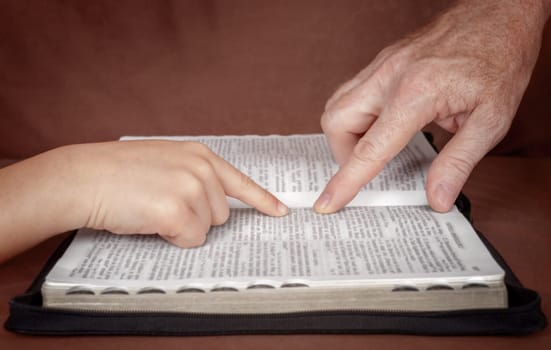 Hand of man pointing something to a child in the Bible book. Teaching a disciple from the Bible.