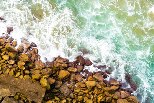 Top aerial view of blue waves crashing on rocky Australian coastline. Summer seascape with birds eye view shot over ocean waves and cliffs. Travel concept background