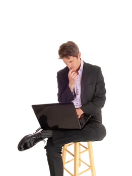 A handsome young business man sitting in a dark suit on a chair with.his laptop on his lap, wondering, isolated for white background.