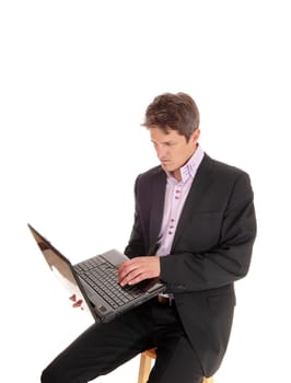 A serious young business man sitting in a suit with his laptop on this lap.typing on the Keyport, isolated for white background.