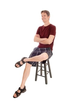 A handsome very happy young man in shorts with his arms crossed.sitting on a chair smiling, isolated for white background.
