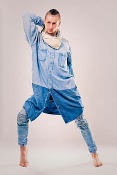caucasian male dancer wearing blue denim shirt and pants on light background performing hip hop and contemporary style dance.