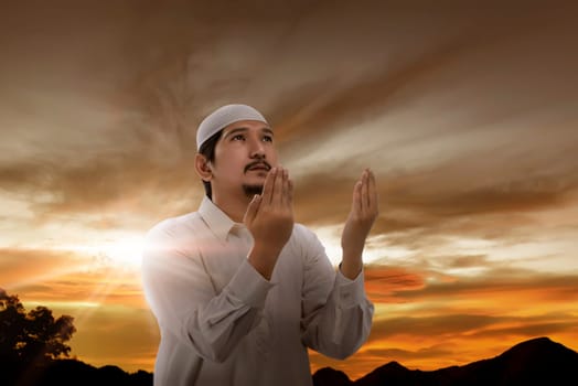 Handsone asian muslim man raising hand and pray during sunset