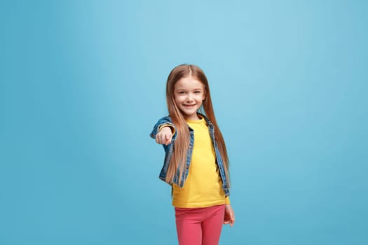 I choose you and order. The smiling teen girl pointing to camera, half length closeup portrait on blue studio background. The human emotions, facial expression concept. Front view. Trendy colors