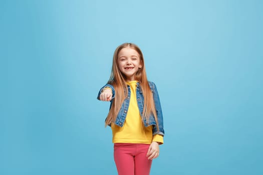 I choose you and order. The smiling teen girl pointing to camera, half length closeup portrait on blue studio background. The human emotions, facial expression concept. Front view. Trendy colors