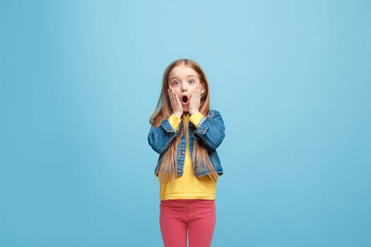 Wow. Beautiful female half-length front portrait isolated on blue studio backgroud. Young emotional surprised teen girl standing with open mouth. Human emotions, facial expression concept. Trendy colors