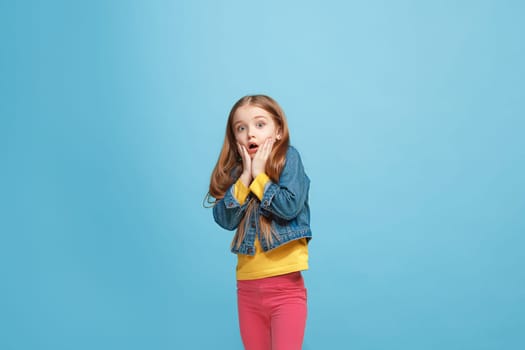 Wow. Beautiful female half-length front portrait isolated on blue studio backgroud. Young emotional surprised teen girl standing with open mouth. Human emotions, facial expression concept. Trendy colors