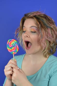 portrait of a young blond woman with colourful hair looking happy at a big lollipop in her hands and thinking about biting into it