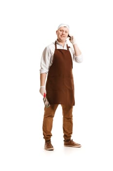 Smiling butcher posing with a knife and mobile phone isolated on white studio background. The young caucasian male model in full-length. Butcher, knife, professional concept