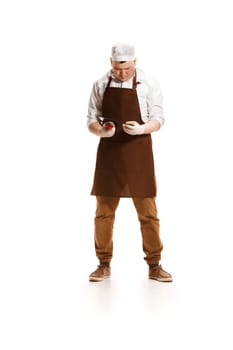 Sad butcher posing with a knife and mobile phone isolated on white studio background. The young caucasian male model in full-length. Butcher, knife, professional concept
