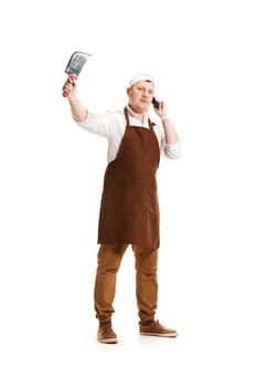 Smiling butcher posing with a knife and mobile phone isolated on white studio background. The young caucasian male model in full-length. Butcher, knife, professional concept