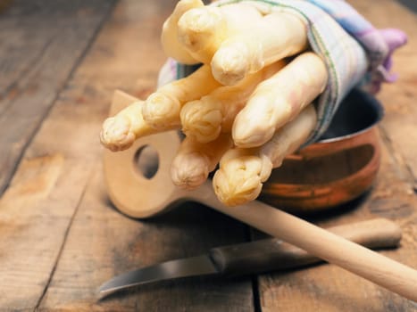 Raw organic white asparagus on a rustic wooden kitchen table, healthy or seasonal food