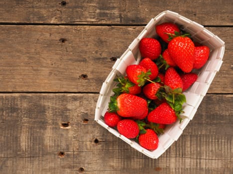 Fresh organic strawberries in a white basket on a rustic wooden table