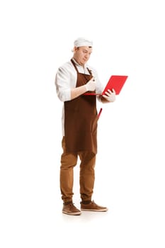 Serious butcher posing with a laptop isolated on white studio background. The young caucasian male model in full-length. Butcher, professional concept