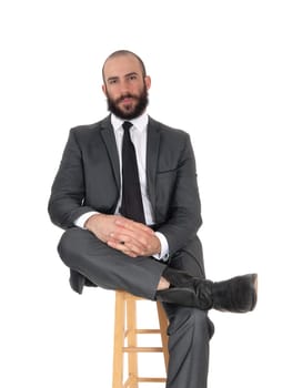 A young looking handsome businessman sitting on a bar chair with his.legs crossed with a beard and mustache, isolated for white background.