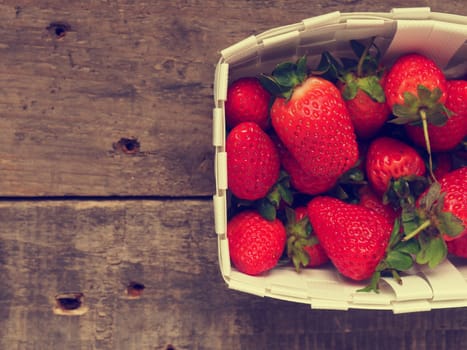 Fresh organic strawberries in a white basket on a rustic wooden table