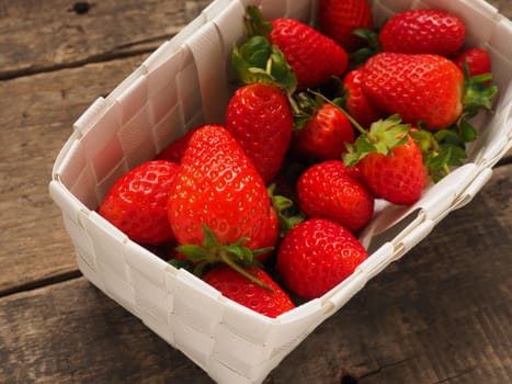Fresh organic strawberries in a white basket on a rustic wooden table