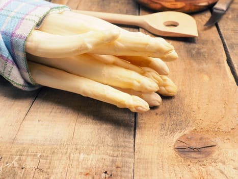 Raw organic white asparagus on a rustic wooden kitchen table, healthy or seasonal food