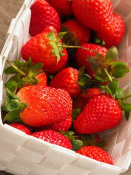 Fresh organic strawberries in a white basket on a rustic wooden table