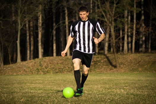 The football player or soccer player is playing football outdoors in the park.