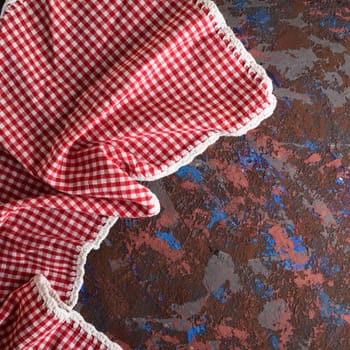kitchen textile napkin in a red and white cell on a brown textured surface, copy space