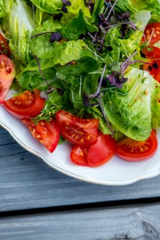 mixed summer salad on plate and wooden ground