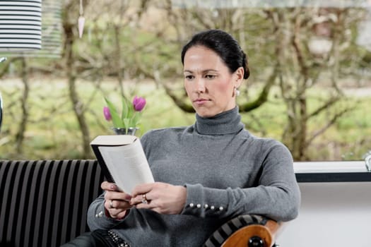 young dark haired woman at home relaxing and reading book