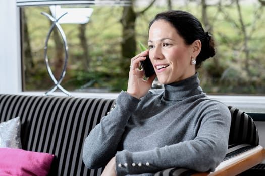 young dark haired woman at home sitting on sofa and calling