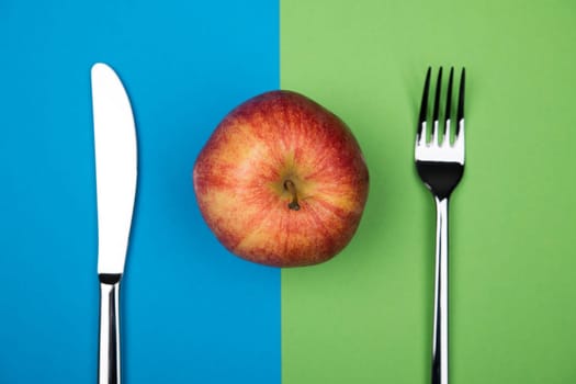 red apple from above with knife and fork on blue and green ground
